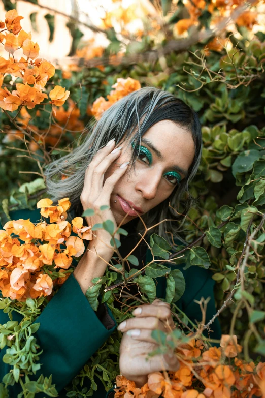 a woman in a green coat surrounded by orange flowers, inspired by Elsa Bleda, trending on pexels, oona chaplin, tanned ameera al taweel, an overgrown, jade colored eyes