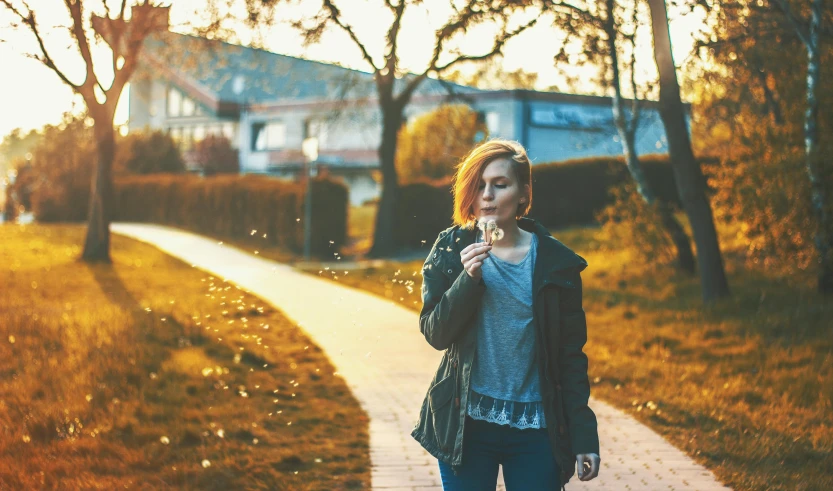 a woman standing on a sidewalk blowing bubbles, by Niko Henrichon, pexels contest winner, realism, girl with a flower head, melancholy autumn light, walking through a suburb, a redheaded young woman