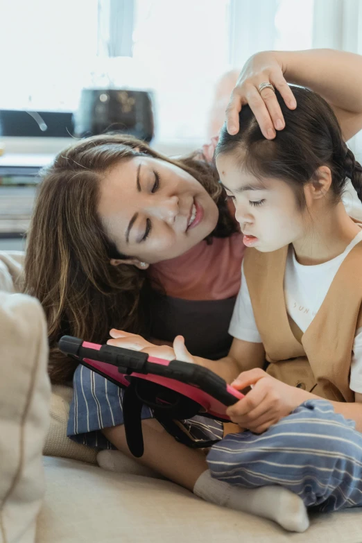 a woman and a little girl sitting on a couch, pexels contest winner, incoherents, using a magical tablet, asian features, touching heads, schools
