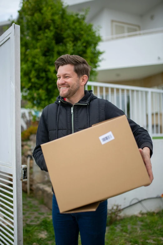 a man holding a box in front of a house, profile image, large, brown, ecommerce photograph