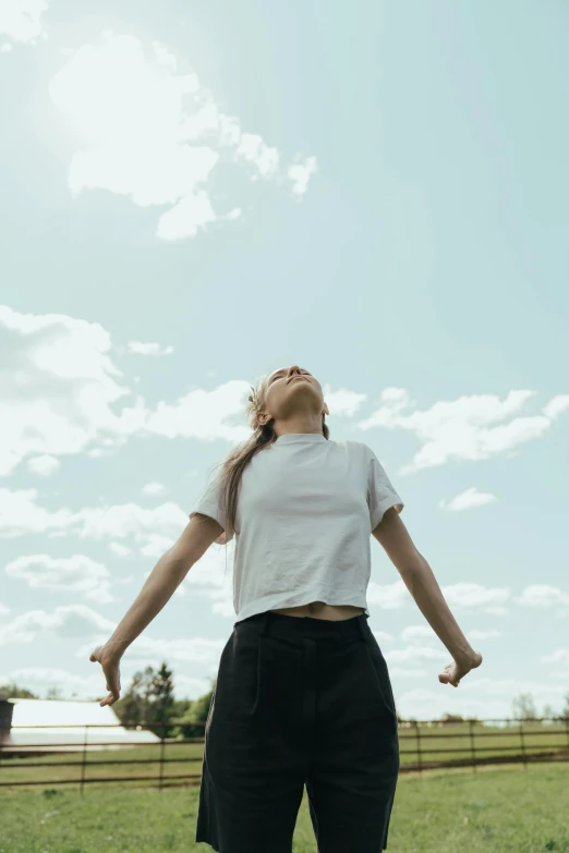 a woman standing on top of a lush green field, dressed in a white t shirt, face looking skyward, kailee mandel, supportive