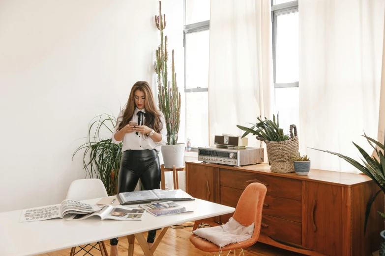 a woman standing in a living room holding a camera, by Nicolette Macnamara, trending on unsplash, happening, table with microphones, urban jungle plants, white table, set inside of office