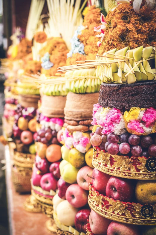 a row of baskets filled with lots of different types of fruit, standing in a hindu kovil, bali, cake, wrapped in flowers