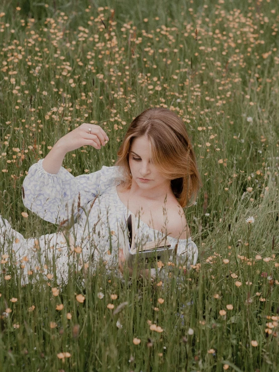 a woman laying in a field of tall grass, inspired by Elsa Bleda, trending on unsplash, holding a book, 🌸 🌼 💮, slightly pixelated, in a cottagecore flower garden