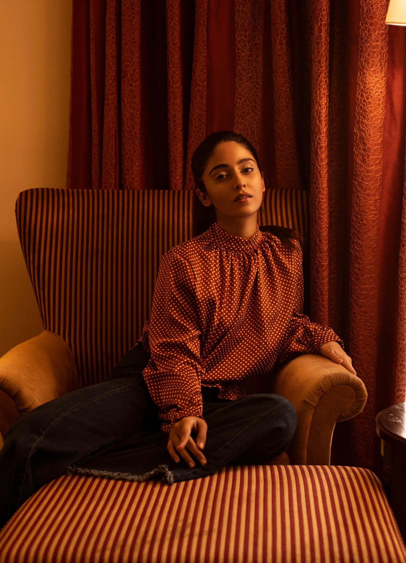 a woman sitting in a chair next to a lamp, imaan hammam, red shirt brown pants, hotel room, ritu kumar