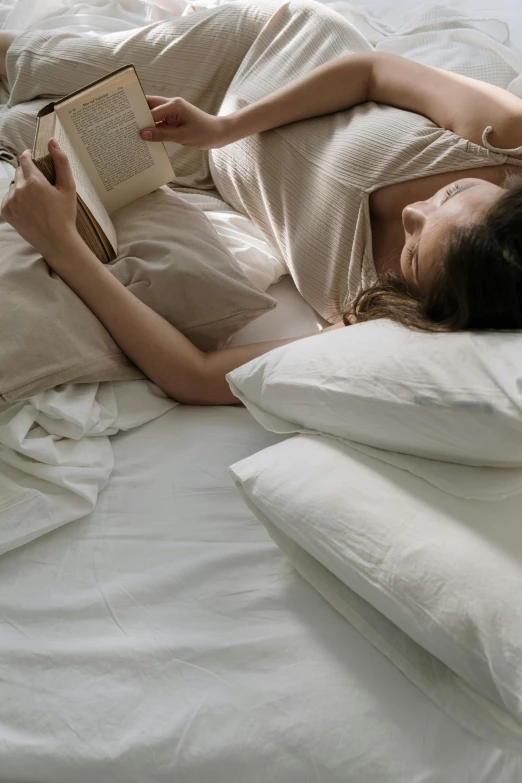 a woman laying in bed reading a book, inspired by Elsa Bleda, happening, light beige pillows, top down angle, bedhead, soft shade