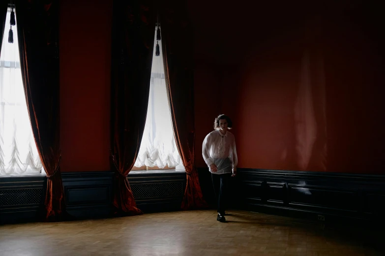 a man standing in front of two large windows, an album cover, inspired by Anna Füssli, baroque, red room, mat collishaw, photographed for reuters, a woman walking