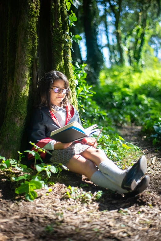 a woman sitting under a tree reading a book, wearing a school uniform, girl walking in forest, she wears harry potter glasses, woodland location