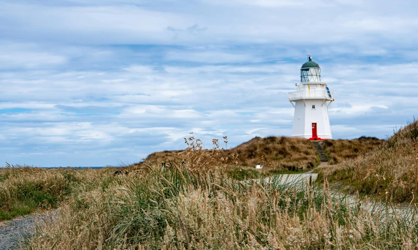 a white and red lighthouse sitting on top of a hill, by Peter Churcher, unsplash, new zeeland, square, sand banks, a cozy