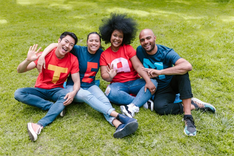 a group of people sitting on top of a lush green field, rated t for teen, red and blue garments, graphic tees, te pae