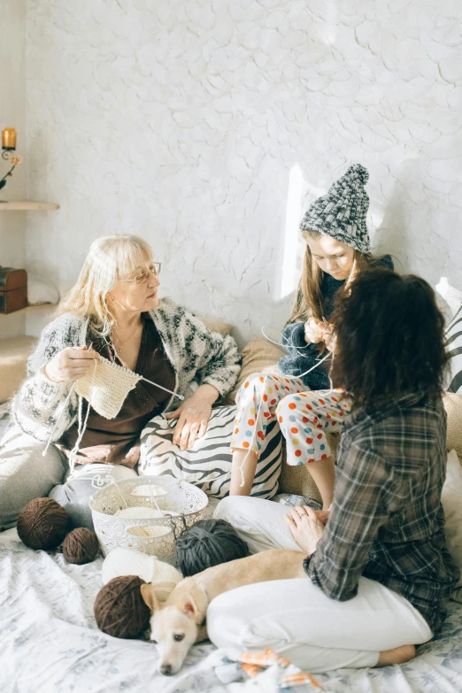 a group of women sitting on top of a bed, a cross stitch, trending on pexels, knitted hat, conversation pit, grey, family