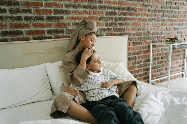 a woman sitting on top of a bed next to a child, pexels, wearing a grey robe, with brown skin, teenage boy, multiple stories