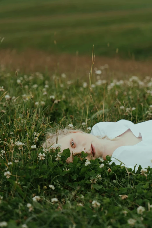 a little girl laying on top of a lush green field, inspired by Elsa Bleda, unsplash, magic realism, extremely pale white skin, ignant, color footage, hyperrealistic aesthetic