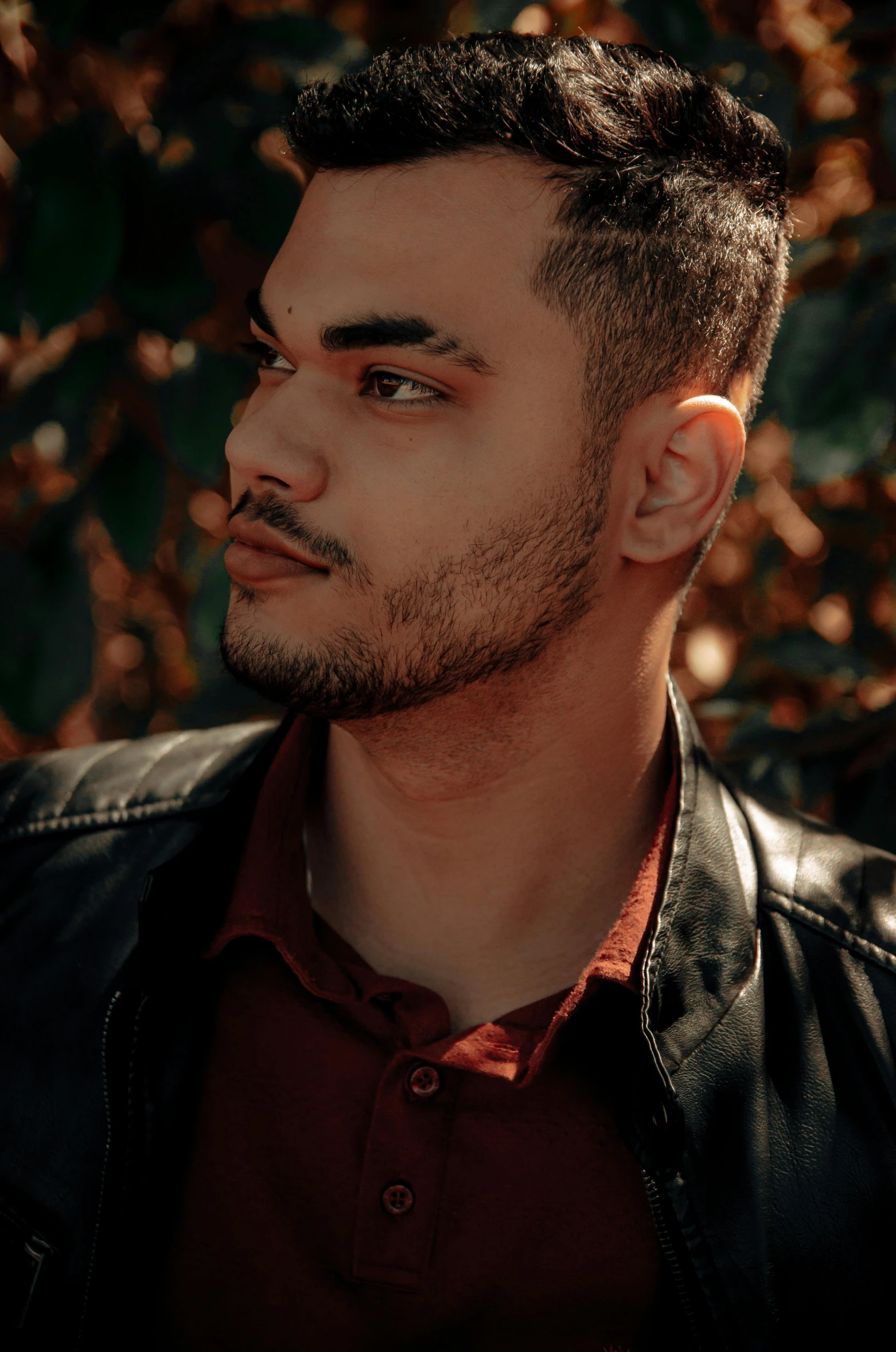 a close up of a person wearing a leather jacket, an album cover, pexels contest winner, middle eastern skin, light stubble with red shirt, lush surroundings, ((portrait))