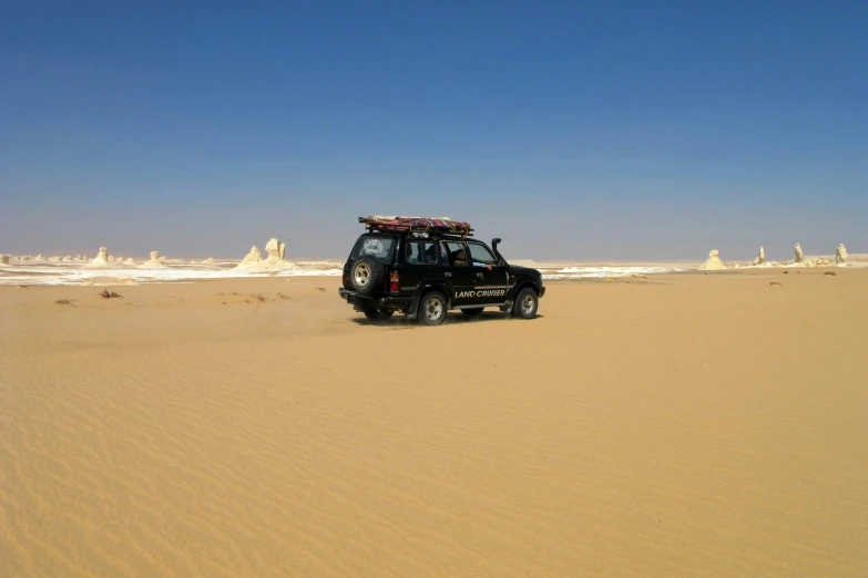 a car that is sitting in the sand, les nabis, egyptian atmosphere, 1km tall, surrounding the city