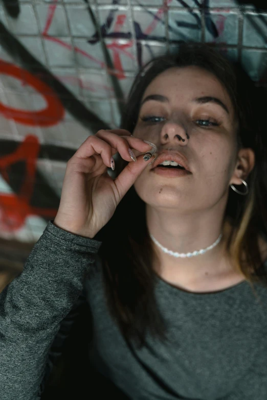 a woman smoking a cigarette in front of a graffiti covered wall, inspired by Elsa Bleda, trending on pexels, wearing choker, pills, portrait of depressed teen, looking at the ceiling