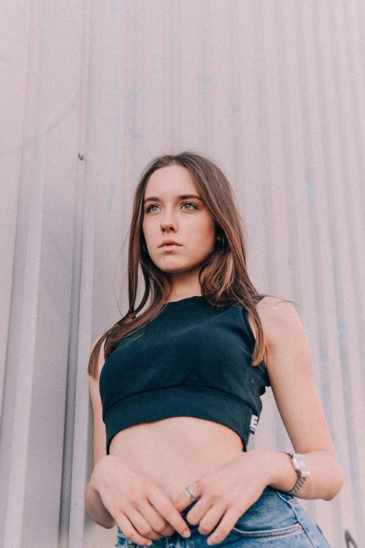 a woman standing in front of a metal wall, an album cover, unsplash contest winner, wearing a cropped black tank top, portrait sophie mudd, wearing fitness gear, concerned expression