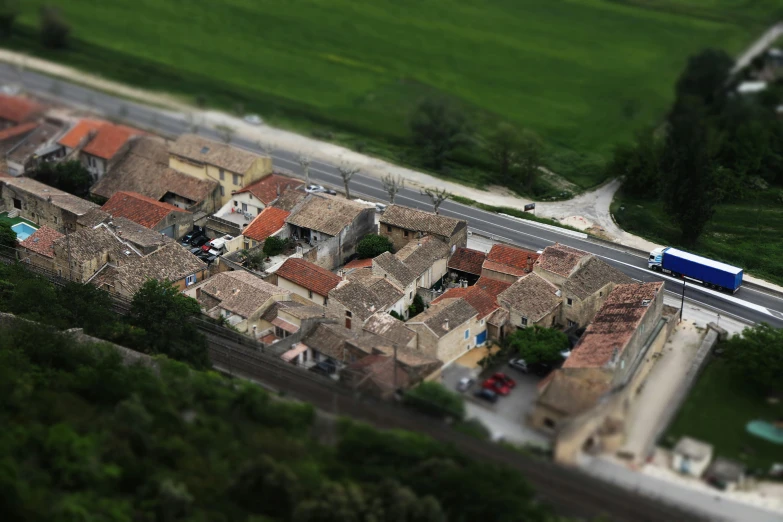a train traveling through a small town next to a lush green field, a tilt shift photo, pexels contest winner, photorealism, lourmarin, tiled roofs, museum photo, built on a small