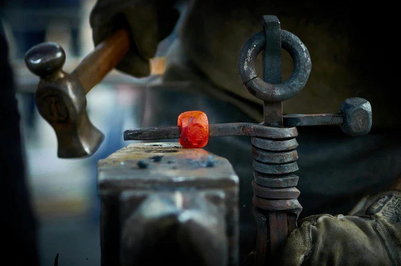 a man working on a piece of metal with a hammer, by Adam Marczyński, pexels contest winner, glass pipes showing red, wrought iron, statue of a cubes and rings, steel mill