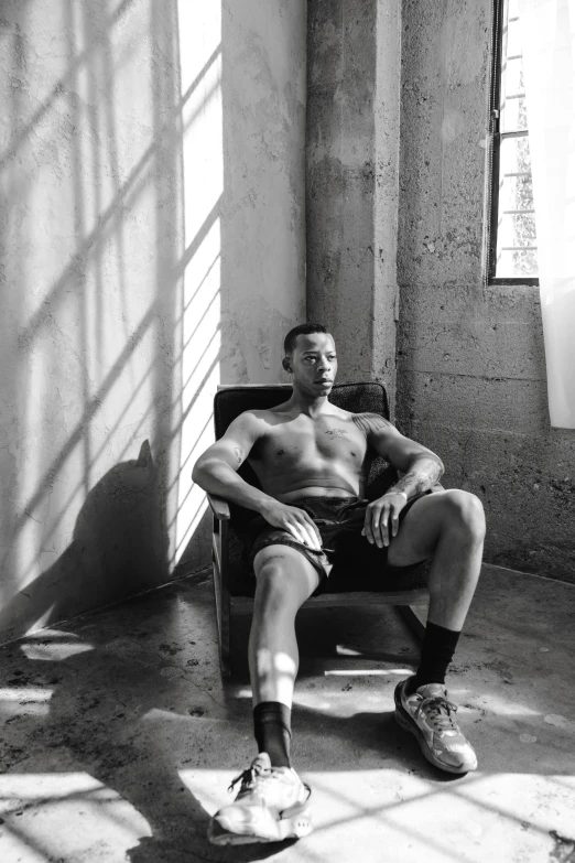 a black and white photo of a man sitting in a chair, inspired by Gordon Parks, renaissance, sweaty abs, sun behind him, gustavo fring, in a warehouse