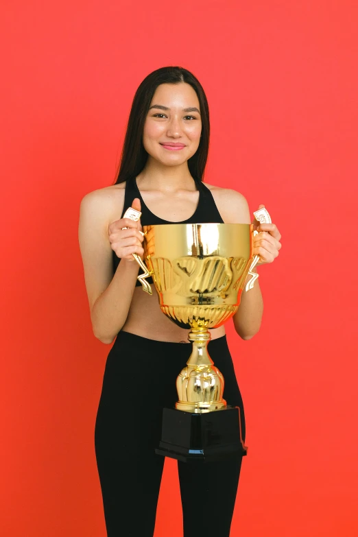 a woman holding a trophy in front of a red background, pexels contest winner, beautiful young asian woman, set against a white background, sports, “ golden cup