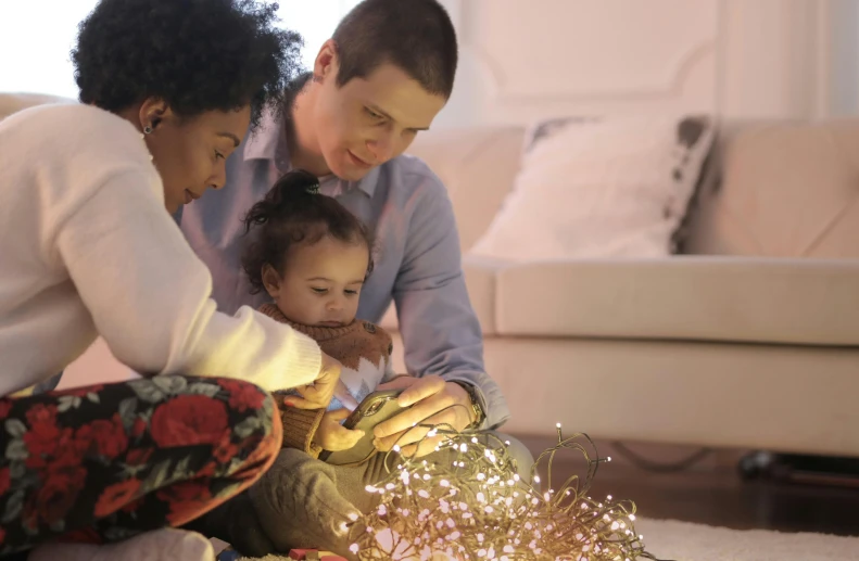 a woman and child sitting on the floor in front of a christmas tree, firefly lights, husband wife and son, flowers around, with sparking circuits