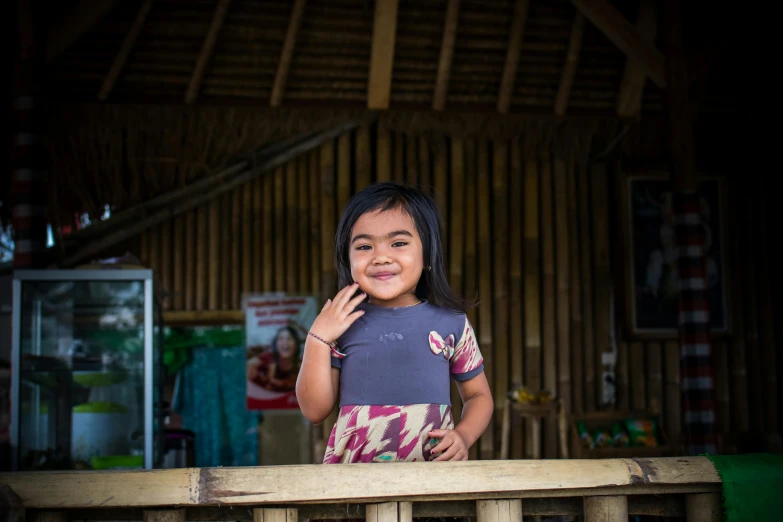 a little girl standing on top of a wooden bench, a portrait, pexels contest winner, sumatraism, avatar image, south east asian with round face, medium-shot, frontal shot