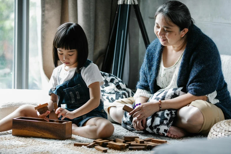 a woman and a little girl sitting on the floor, pexels contest winner, arts and crafts movement, wooden art toys, an asian woman, building blocks, youtube thumbnail