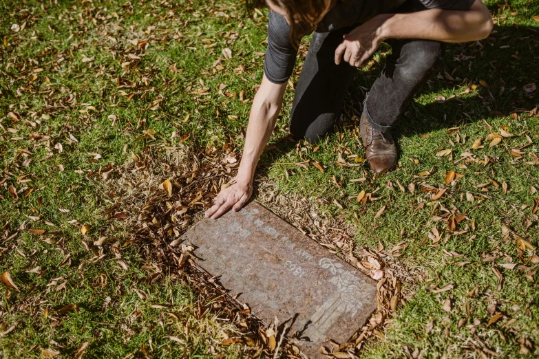 a woman kneeling on top of a grass covered field, by Gwen Barnard, unsplash, auto-destructive art, standing over a tomb stone, william eggleston, holding a wood piece, discovered for the first time