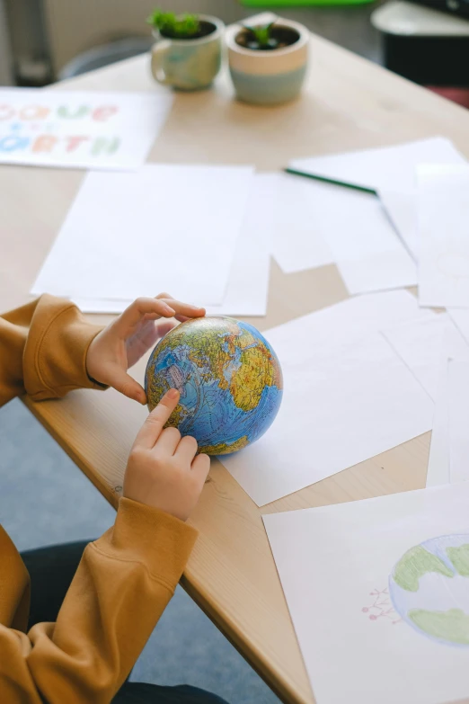 a little boy that is sitting at a table with a globe, a child's drawing, trending on pexels, sustainable materials, middle shot, barometric projection, seen from earth