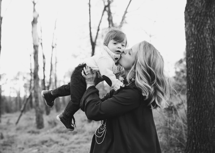 a woman holding a small child in her arms, a black and white photo, pexels, photograph captured in the woods, brandi love, blonde, listing image