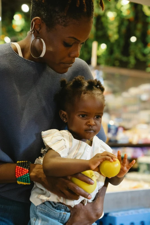 a woman holding a small child in her arms, by Willard Mullin, pexels, stood in a supermarket, african arts, mango, contemplating