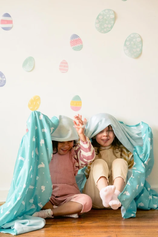 two little girls sitting under a blanket on the floor, a picture, shutterstock contest winner, holding easter eggs, pale cyan and grey fabric, waving, thumbnail