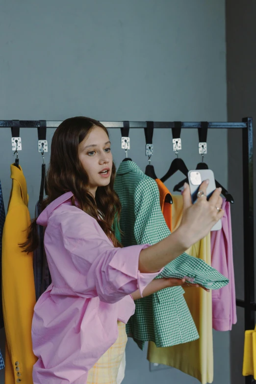 a woman standing in front of a rack of clothes, taking a selfie, mackenzie foy, shot with sony alpha, wearing nanotech honeycomb robe