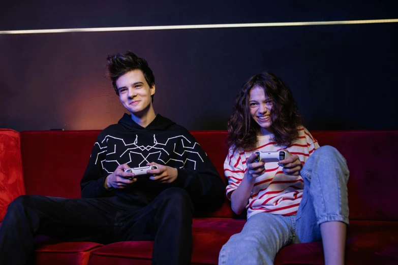 a couple of people sitting on top of a red couch, holding controller, teenagers, promotional image, profile pic