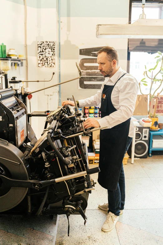 a man working on a motorcycle in a garage, a silk screen, pexels contest winner, private press, helvetica, factory floor, in a studio, style of hr geiger
