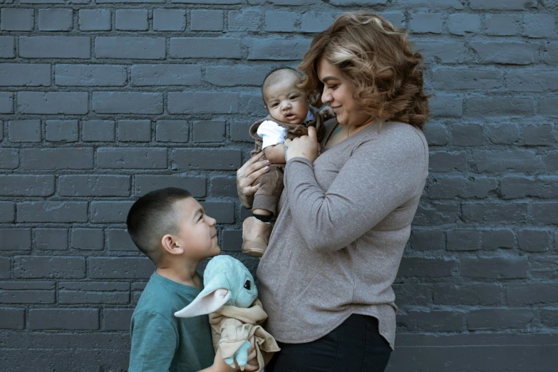 a woman standing next to a boy holding a stuffed animal, pexels contest winner, realism, hispanic, portrait of family of three, profile image, cuddling her gremlings