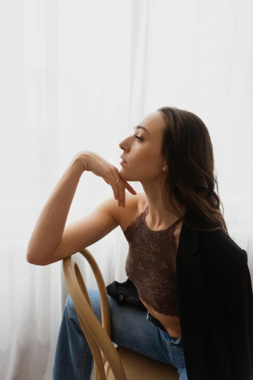 a woman sitting on a chair in front of a window, trending on pexels, arabesque, she is wearing a black tank top, profile image, brown haired, thinking pose