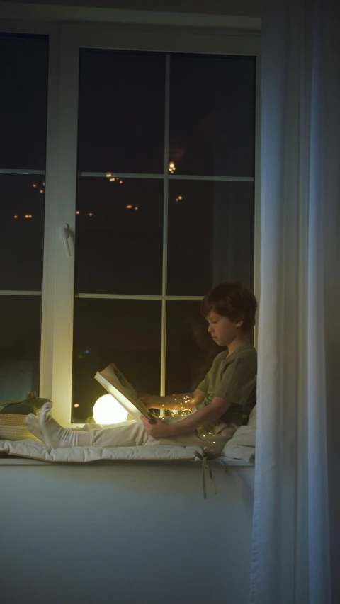 a person sitting on a window sill reading a book, by Gregory Crewdson, pexels, glowing paper lanterns, light over boy, gif