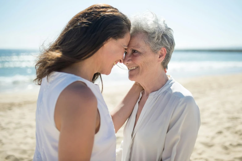 two women standing next to each other on a beach, by Arabella Rankin, unsplash, smiling at each other, older woman, touching heads, very pretty