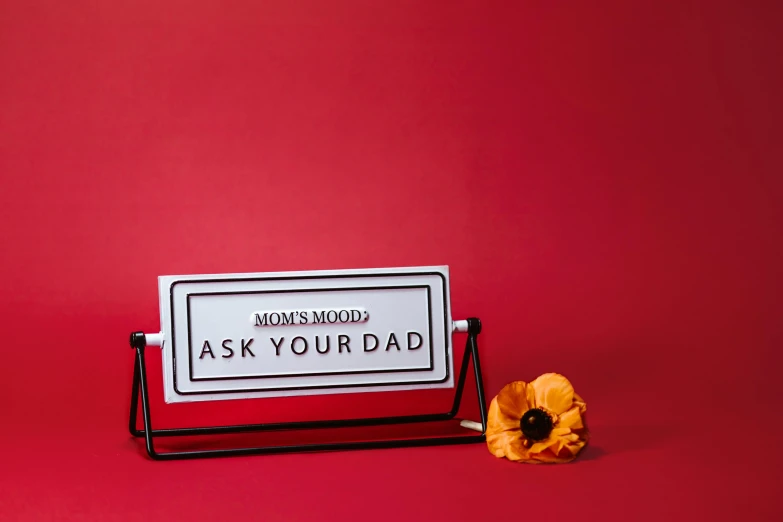 a sign that says ask your dad next to a flower, unsplash, modernism, tabletop model, red and black colour scheme, mummy, card frame