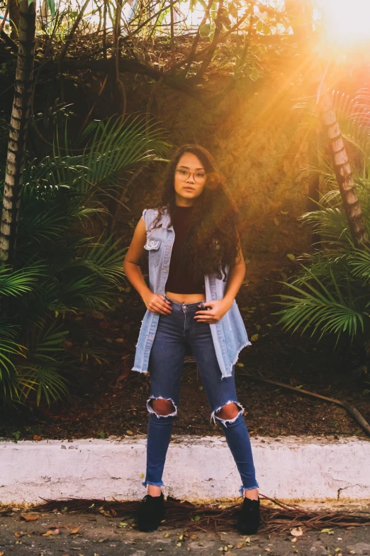 a woman standing in front of a lush green forest, an album cover, by Robbie Trevino, pexels contest winner, ripped jeans, sun down, panoramic centered view of girl, tropical