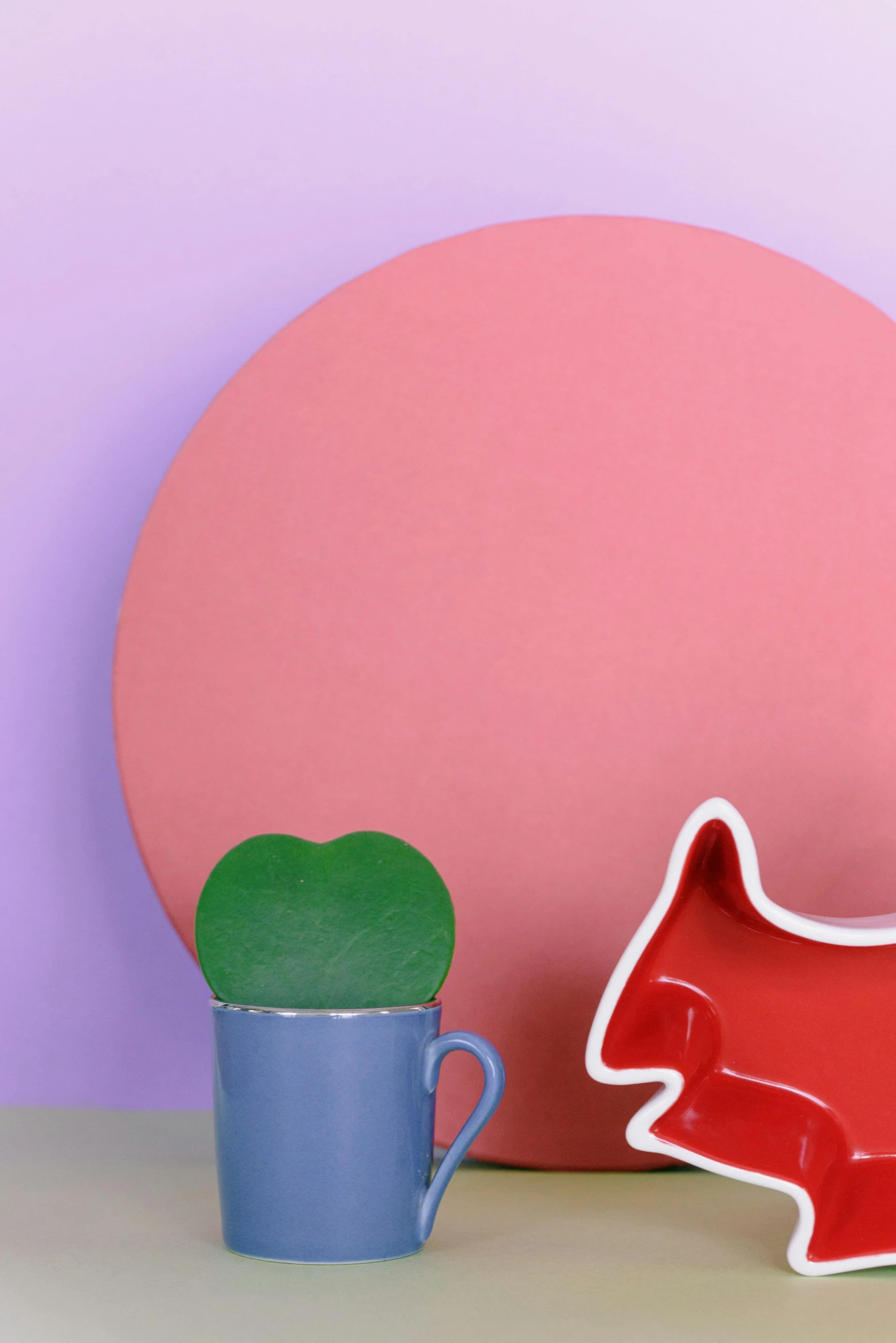 a red dog figurine next to a blue mug, an abstract sculpture, inspired by Tom Wesselmann, trending on pexels, color field, round mirror on the wall, green and purple studio lighting, pink pastel, made of glazed