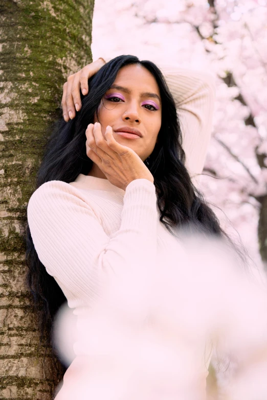 a woman leaning against a tree in a park, an album cover, by Robbie Trevino, trending on pexels, white and light-pink outfit, salma hayek, blossoms, pose 4 of 1 6