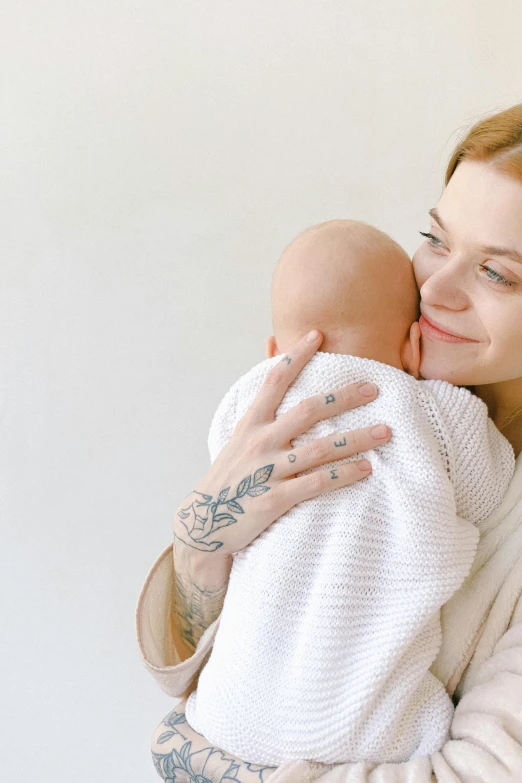 a woman holding a baby in her arms, pexels, antipodeans, on a pale background, profile image, tattooed, skincare