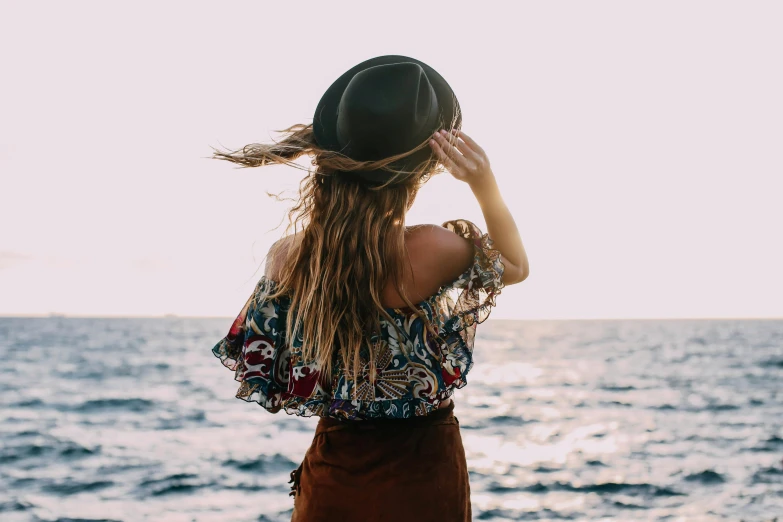 a woman standing on top of a beach next to the ocean, trending on pexels, renaissance, wearing a cute hat, beautiful clothes, back lit, unkept hair