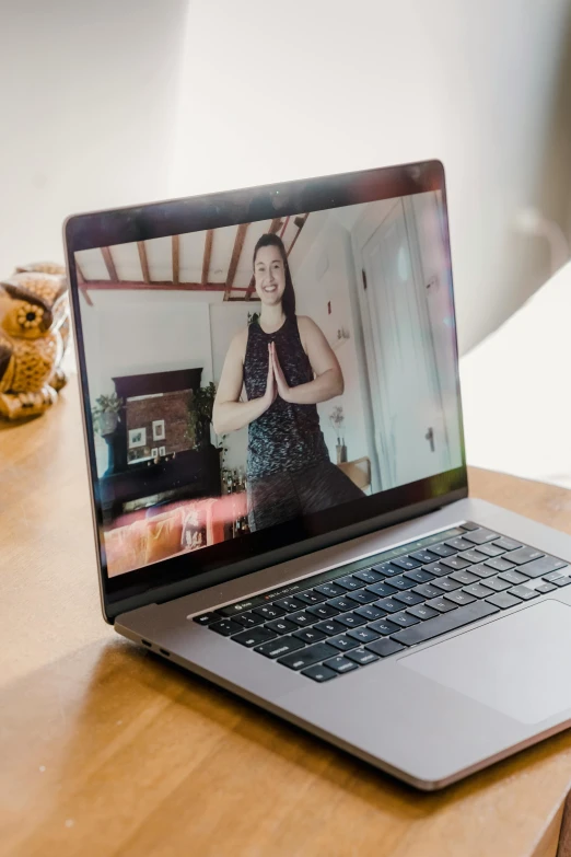 a laptop computer sitting on top of a wooden table, inspired by Li Di, unsplash, video art, dance meditation, looking towards camera, gemma chen, at home