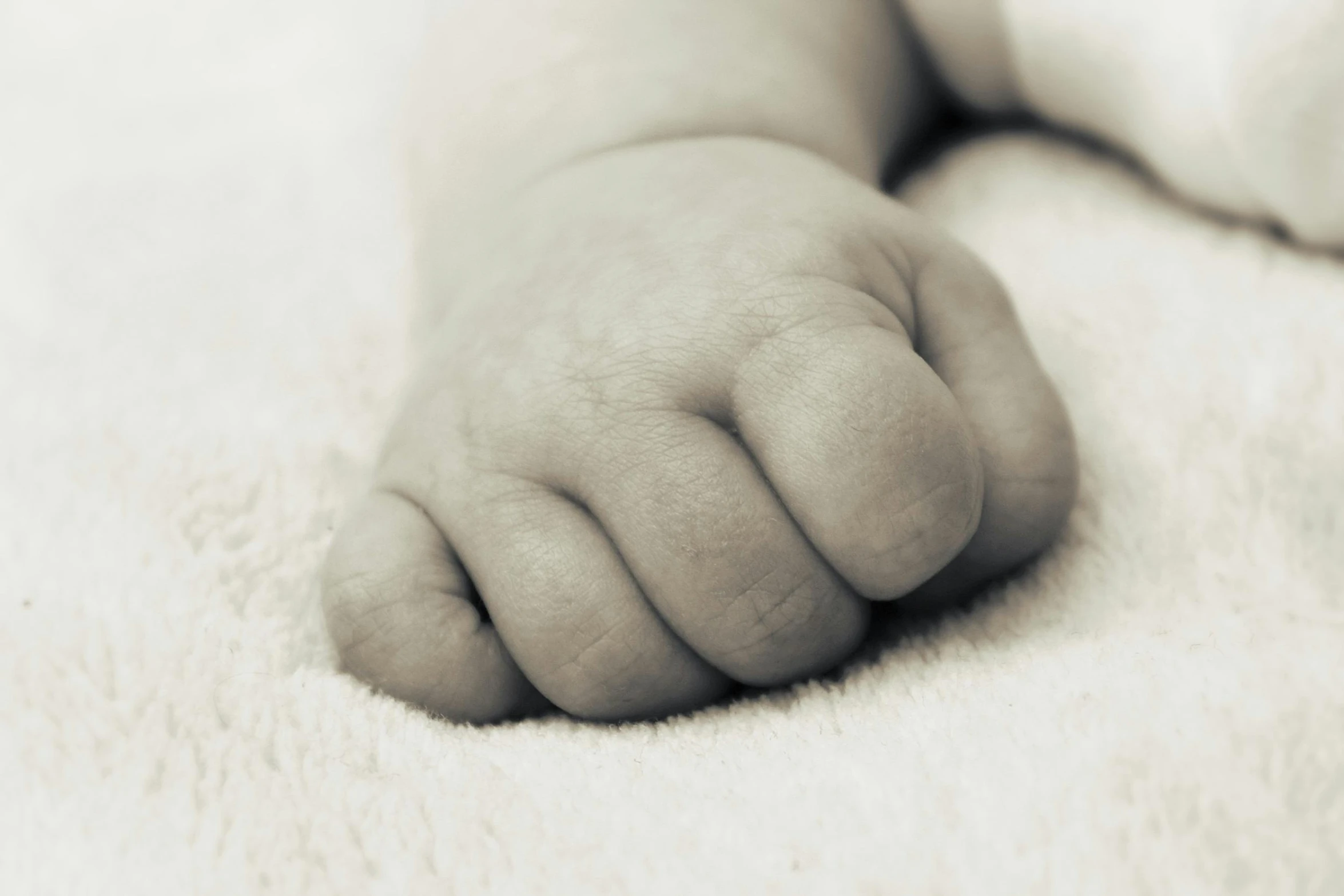 a close up of a baby's hand on a blanket, by Ruth Simpson, unsplash, symbolism, sepia toned, fist training, grey, big feet