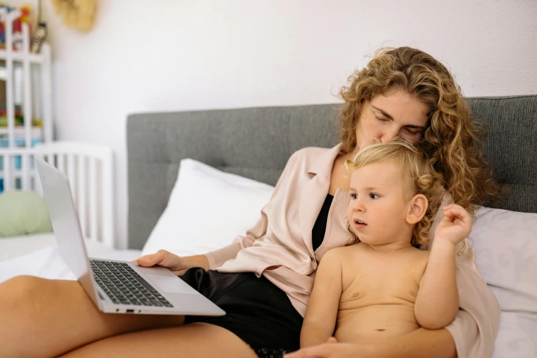 a woman sitting next to a baby on a bed with a laptop, pexels, avatar image, no cropping, a blond, 1 5 0 4