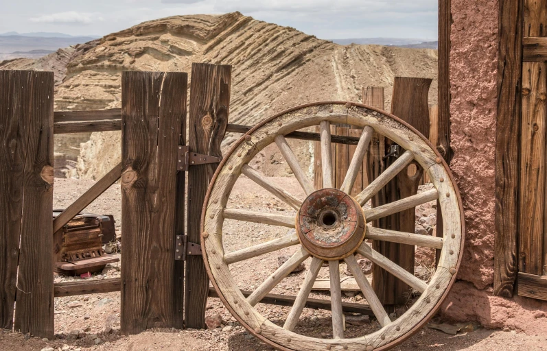 a wooden wagon wheel sitting next to a wooden fence, on the desert, copper veins, rusty vehicles, profile image